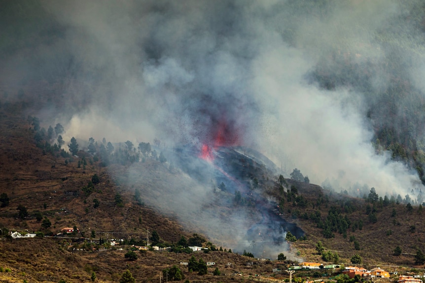 Humo que se eleva desde la ladera de una colina y lava roja en erupción de un volcán