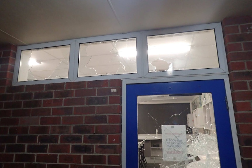 Smashed windows above a smashed glass door at a school.