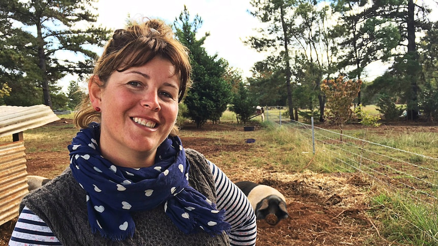 A woman stands next to a fence with pigs in the background.