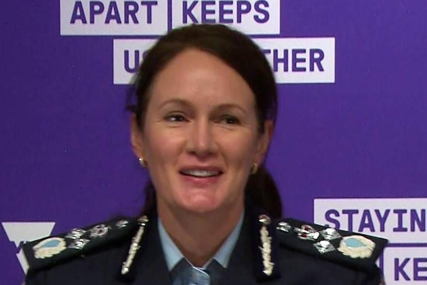 A woman in a uniform in front  of a purple background at a press conference.