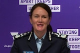 A woman in a uniform in front  of a purple background at a press conference.
