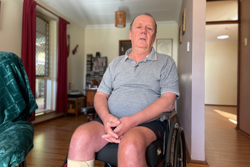 Graham wearing a grey shirt sitting in a wheelchair inside his home.