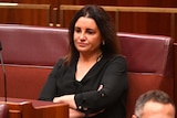 Tasmanian Senator Jacqui Lambie sitting with her arms folded in the Senate chamber.