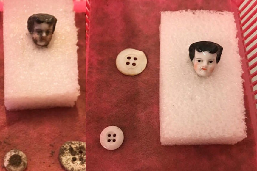 A close up photo of a china doll head with black hair, white skin and rosy pink cheeks. Placed next to a button for scale
