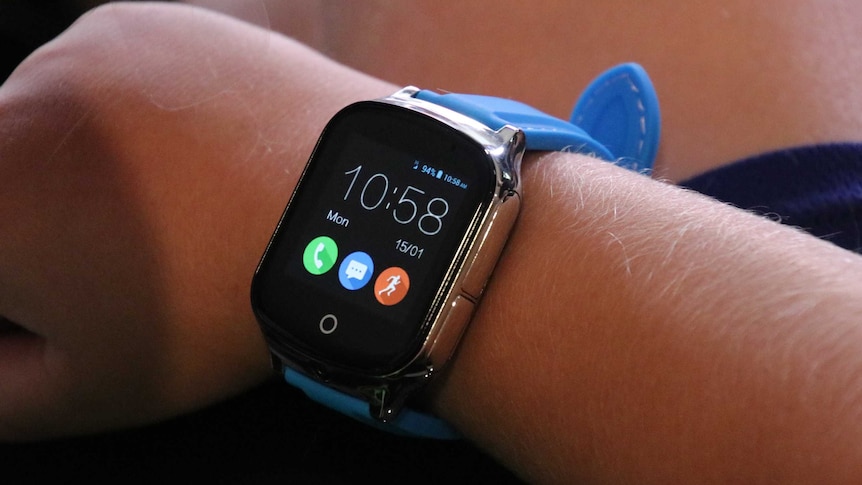 Close up of a child taking the plastic cover off the smart watch he is wearing on his wrist.