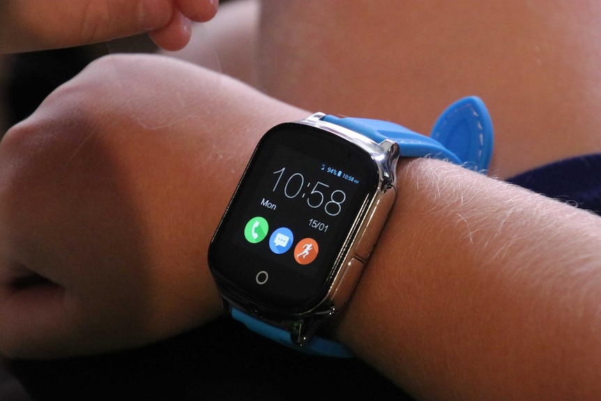 Close up of a child taking the plastic cover off the smart watch he is wearing on his wrist.