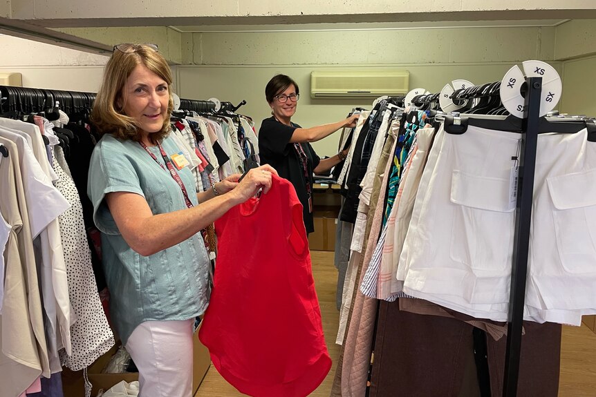 Two women stand near racks of clothing 