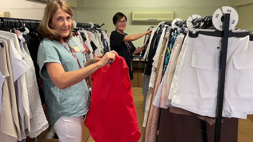 Two women stand near racks of clothing 