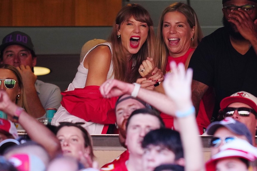 Taylor screams with joy as she grabs the hands of the woman next to her.