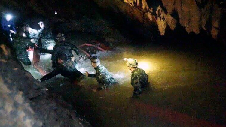 Rescuers inside a dark cave walk through water with headlamps on.