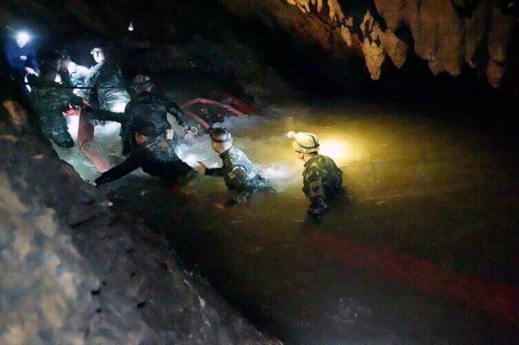 Rescuers inside a dark cave walk through water with headlamps on.