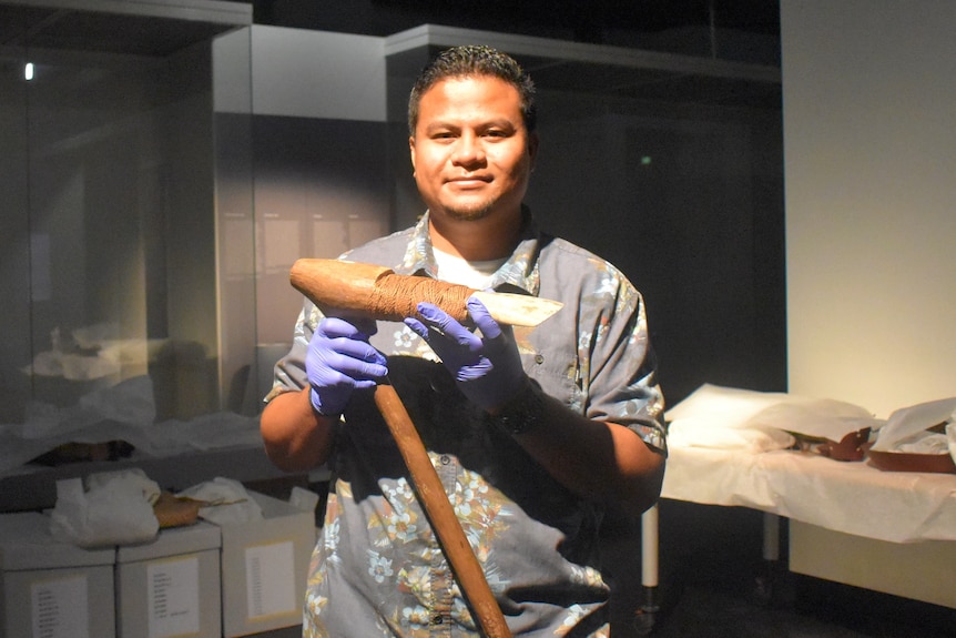 A Palauan man holds a club-like artefact under warm museum lighting 