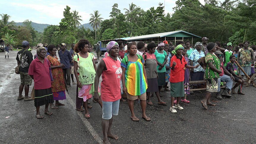 Panguna mine protesters wave their hands and fists in the air and hold a sign that says "No Mining! No BCL!" at a roadblock.