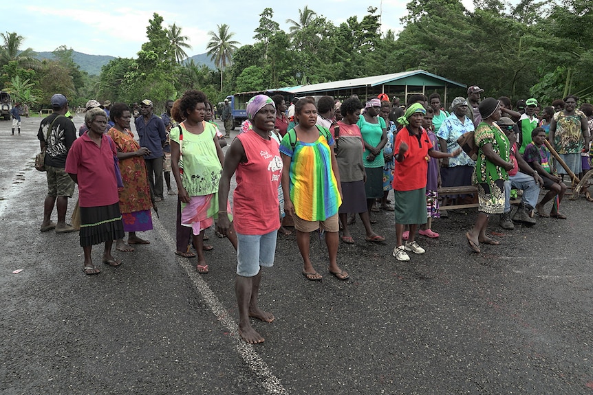 Panguna mine protesters wave their hands and fists in the air and hold a sign that says "No Mining! No BCL!" at a roadblock.