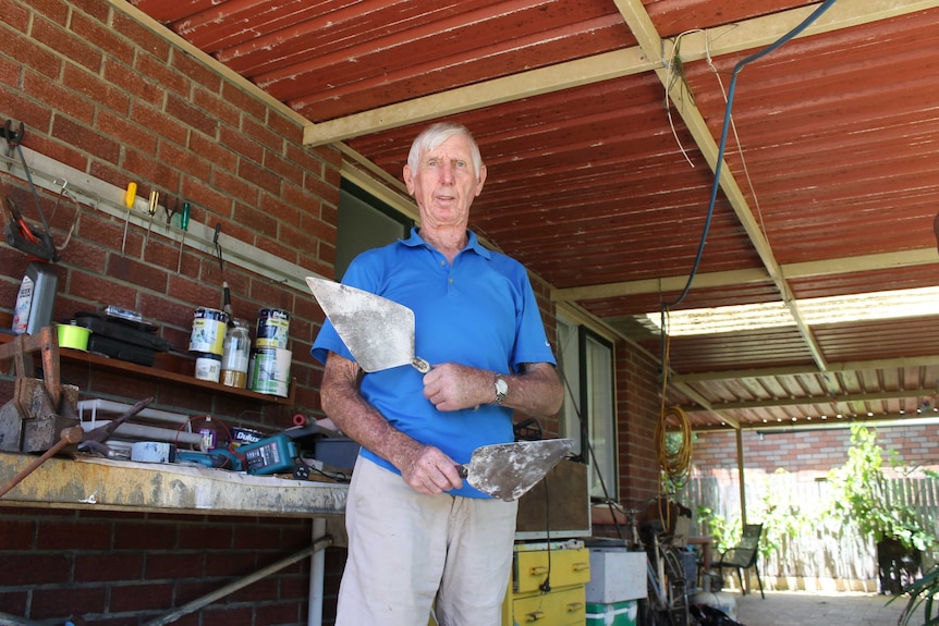Mr Handworth stands in his shed holding two trowels