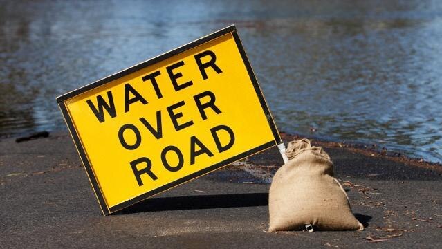 road sign beside laying water, sign text reads "Water over road"