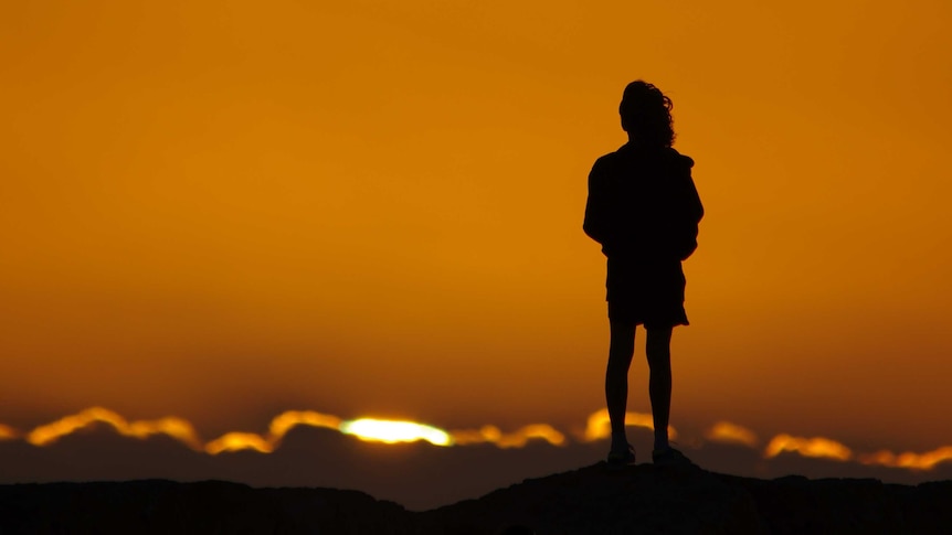 Girl in silhouette watches sunset from rocks