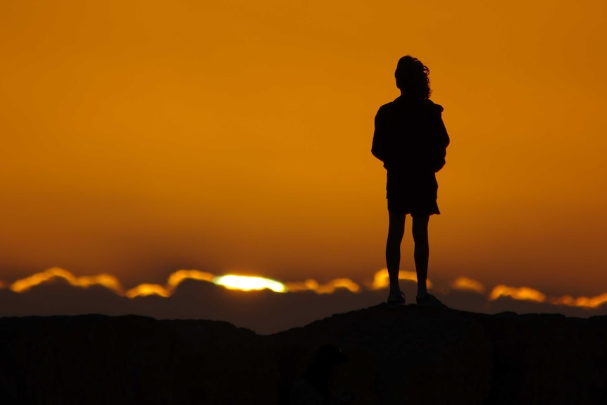 Girl in silhouette watches sunset from rocks