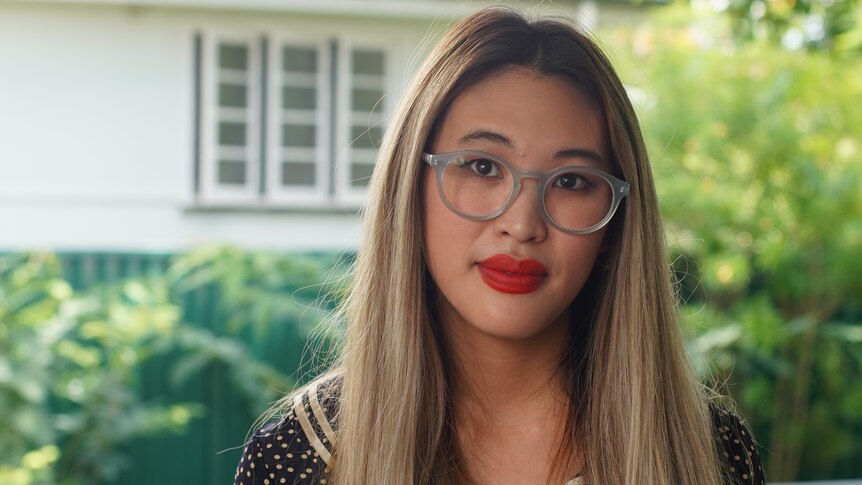 Portrait photo of a woman of Asian descent with light-coloured hair, glasses and red lipstick
