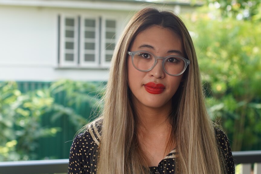 Portrait photo of a woman of Asian descent with light-coloured hair, glasses and red lipstick