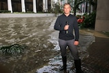 Conor Duffy in gumboots holding a microphone and standing next to floodwaters outside a Miami hotel.