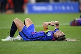 A female soccer player wearing blue and red lays down on the ground
