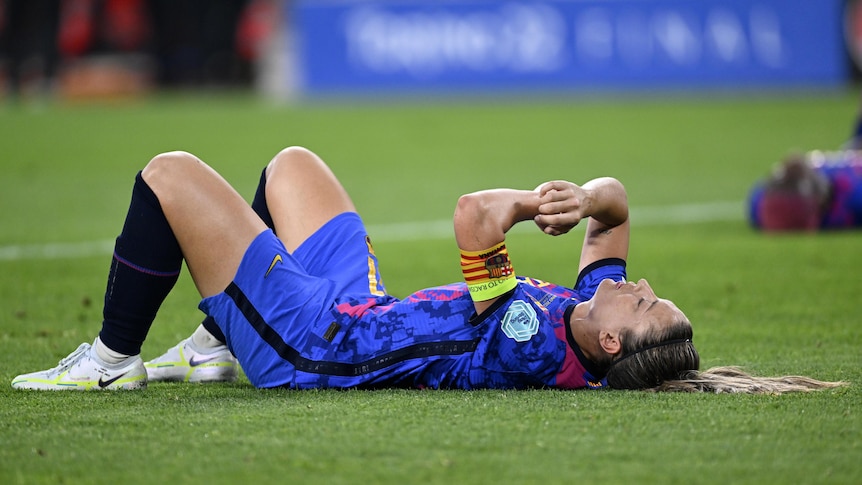 A female soccer player wearing blue and red lays down on the ground