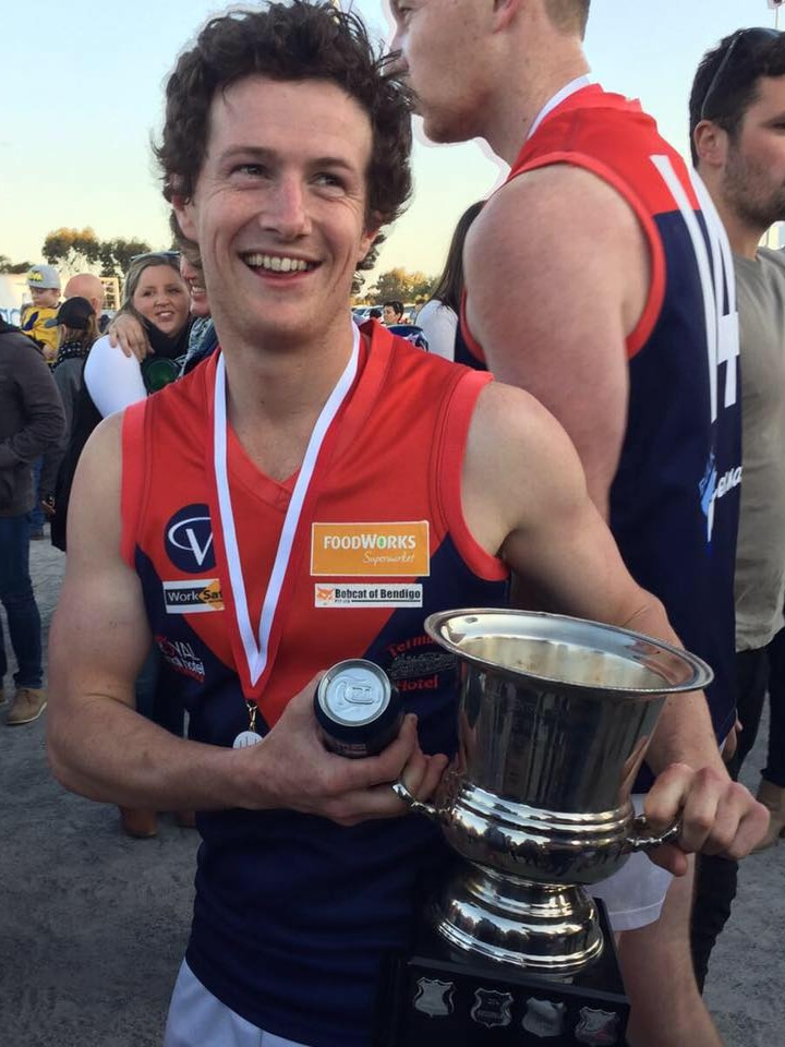 A young man in a football guernsey with a medal around his neck, a beer and a premiership cup in his hands.
