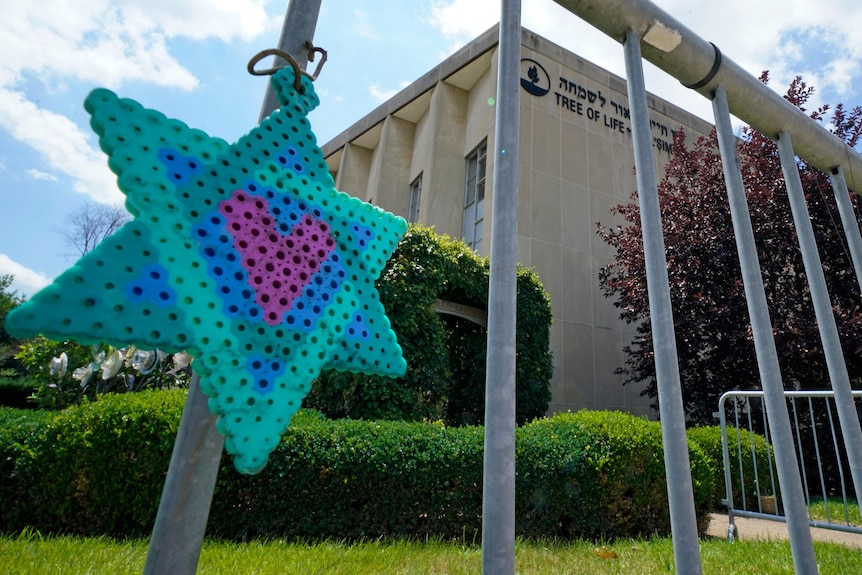 Beaded star of david in pink green and blue hangs on pole outside building 
