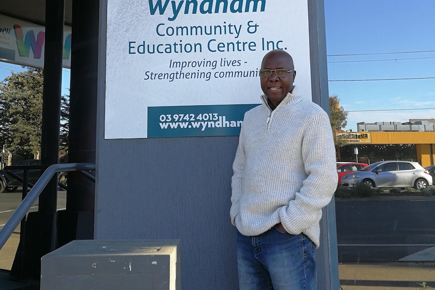 Poly Kiyaga stands in front of a sign on a building that says Wyndham Community and Education Centre.