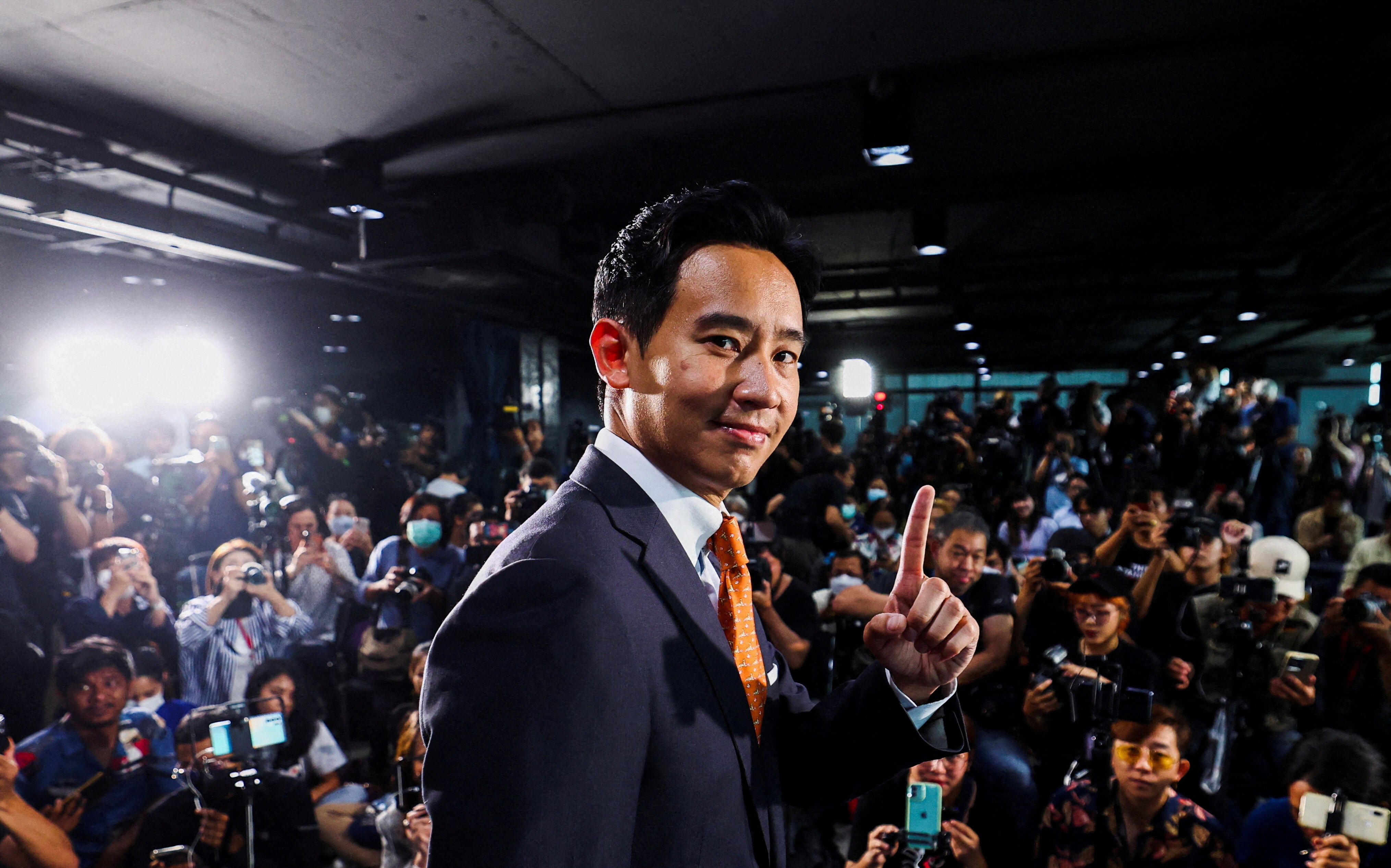 A young Thai man holds up one finger while surrounded by photographers