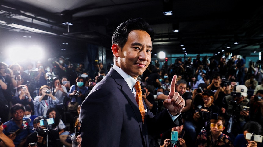 A young Thai man holds up one finger while surrounded by photographers