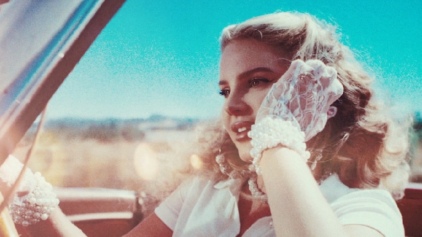 Lana Del Rey, driving vintage convertible, wearing pearls, white top and lace gloves