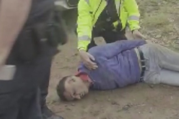 A man on the ground with a police officer assisting him.