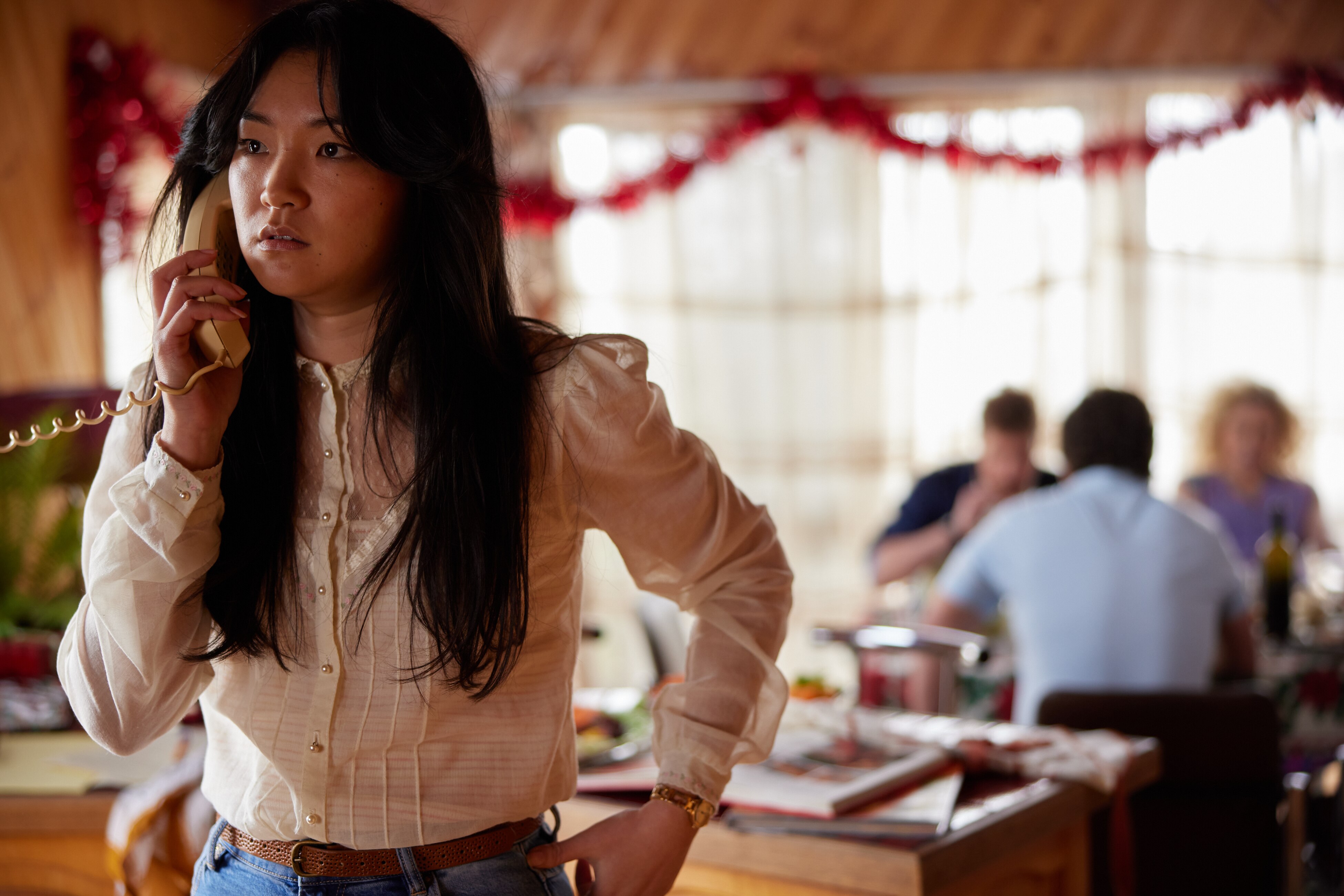 Michelle Lim Davidson as Noelene holding a phone up to her ear