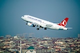 A plane with Turkish Airlines branding flies over a dense cityscape.
