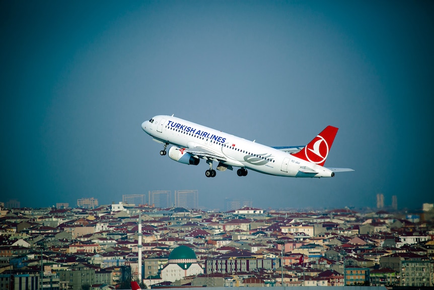 A plane with Turkish Airlines branding flies over a dense cityscape.