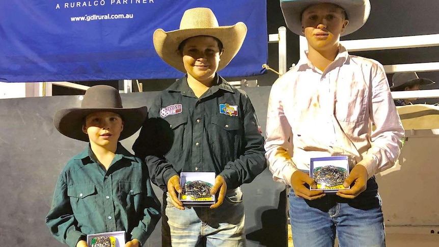 Three rodeo riders stand with their prizes
