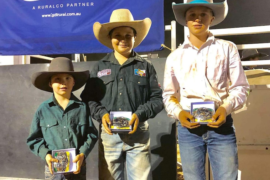 Three rodeo riders stand with their prizes