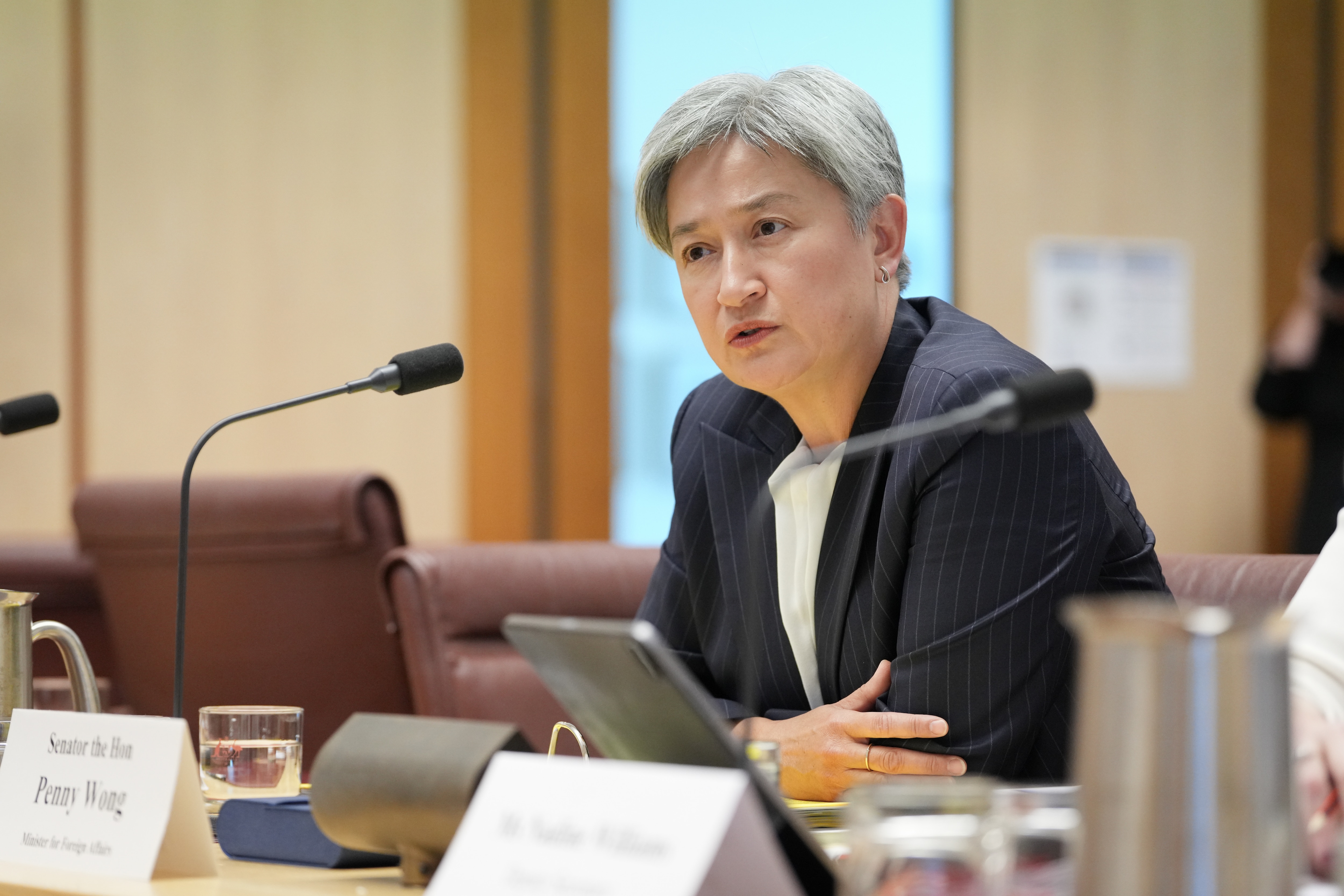 A grey-haired woman in a dark blazer — Penny Wong — sits at a table in a conference room.