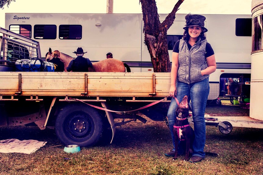 Woman and dog stand next to ute.
