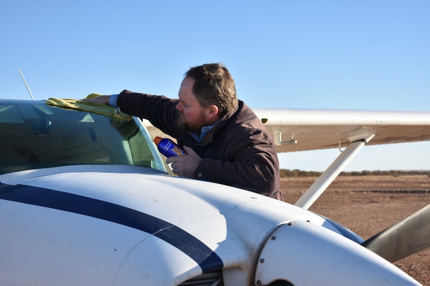 A man wipes clean the windscreen of his light plane with a cloth