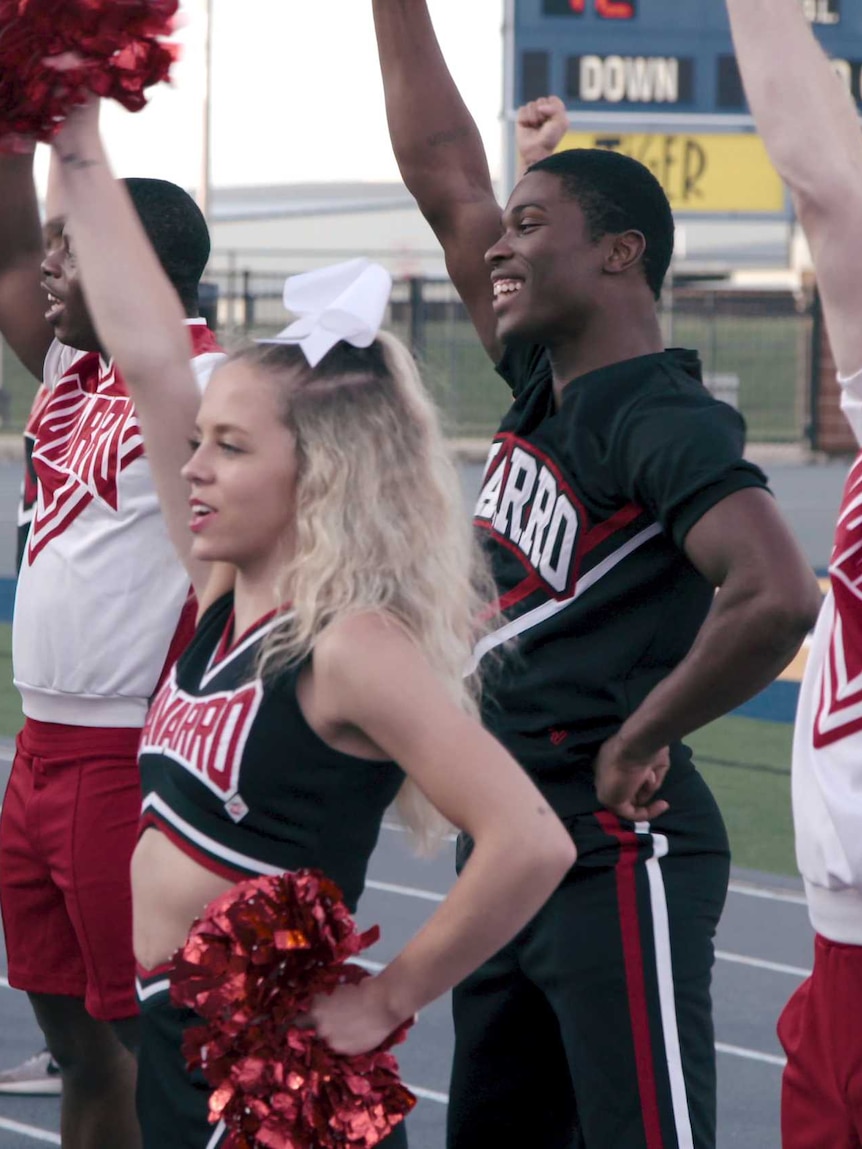 Cheerleaders from Netflix series Cheer with arms raised in the air mid-cheer, in story about cheerleading.