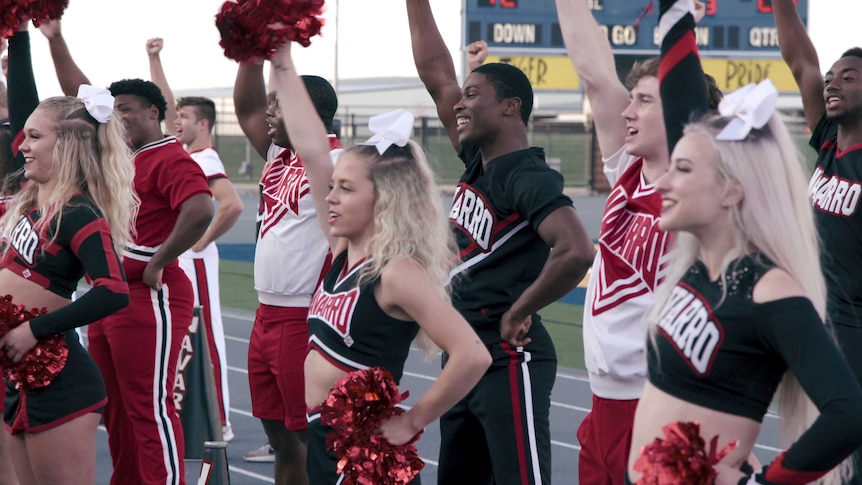 Cheerleaders from Netflix series Cheer with arms raised in the air mid-cheer, in story about cheerleading.