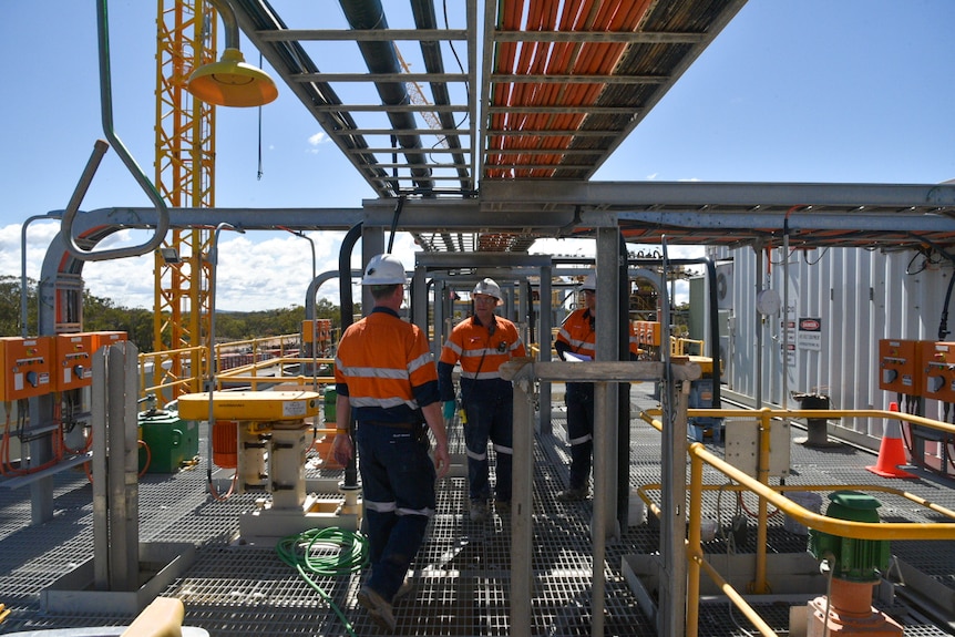 Tres hombres con ropa de trabajo de alta visibilidad se paran en la parte superior de una planta de procesamiento de minería