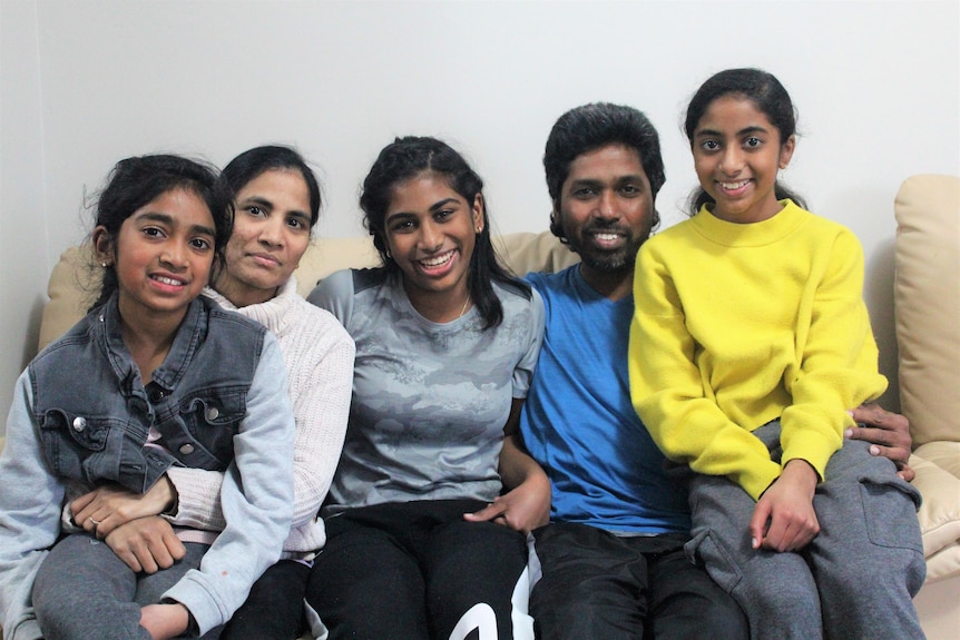 A family sits on a couch with arms around each other 