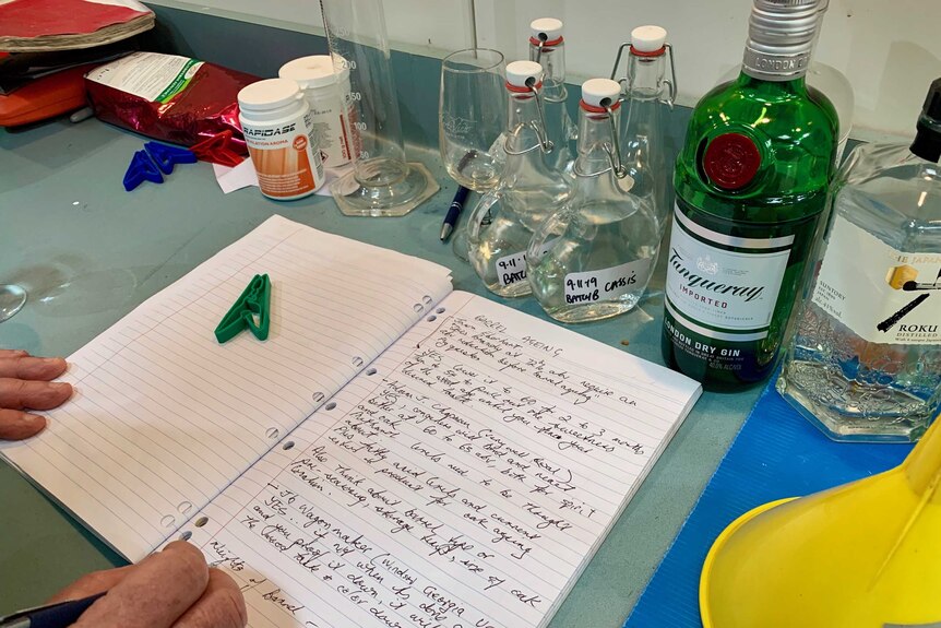 A man is writing on a notebook with different lab equipment and bottles around him