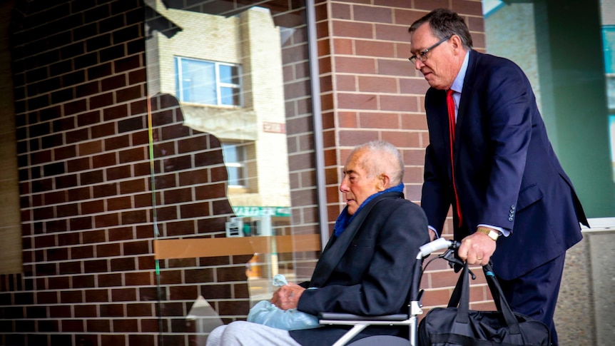 An old man is pushed along outside a court by another man