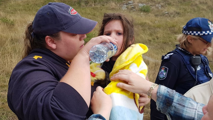 An SES volunteer gives water to a little girl in her arms wrapped in a blanket