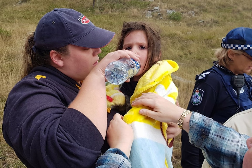 An SES volunteer gives water to a little girl in her arms wrapped in a blanket